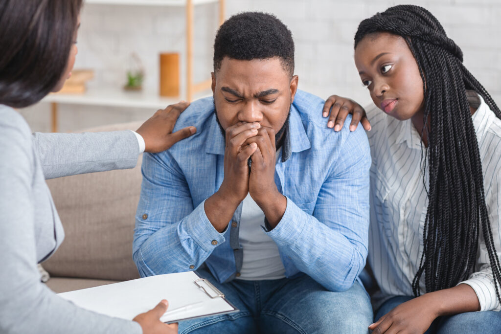 Loving afro wife and unrecognizable psychotherapist supporting guy during therapy session