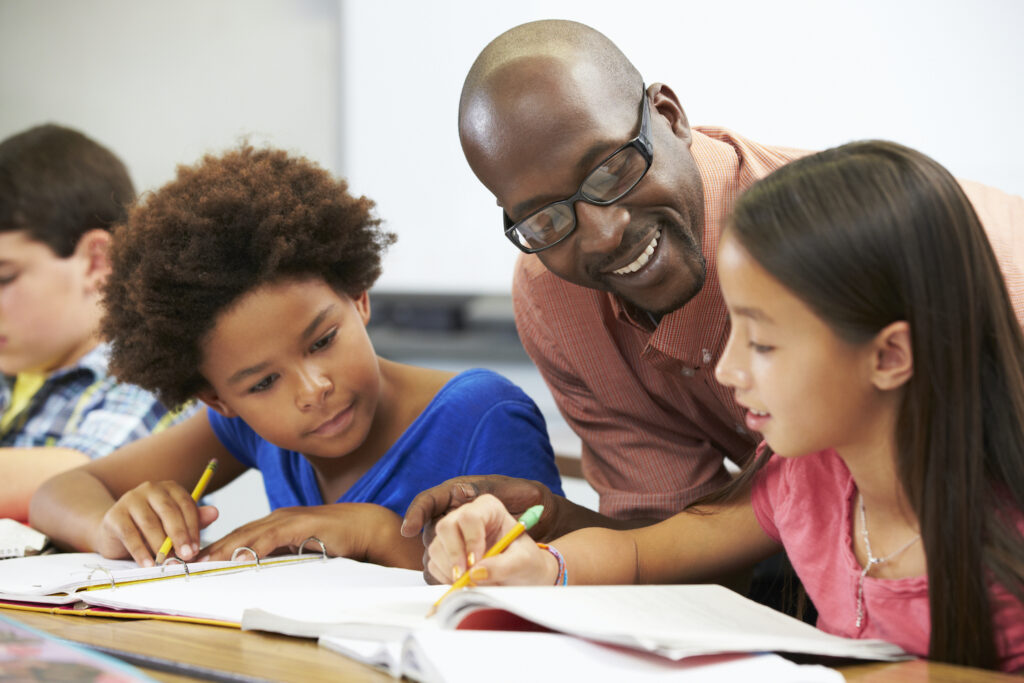 Teacher Helping Pupils Studying At Desks In Classroom